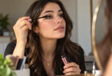Woman applying best waterproof mascara with long, defined lashes and mascara products displayed against a blue water background