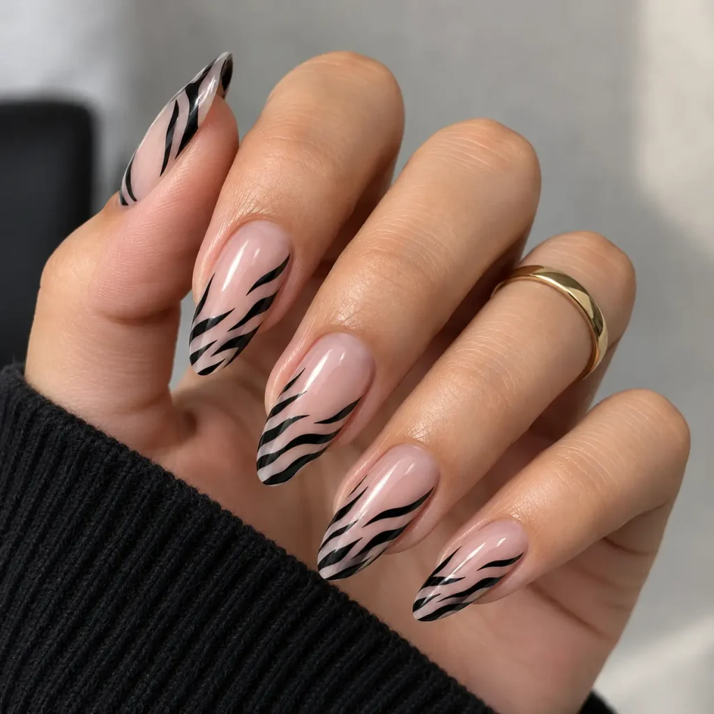 Negative space zebra print nails with a sheer nude-pink base and curved black stripes on glossy almond-shaped nails.